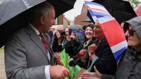 PA Media King Charles talking to well-wishers during his visit to Grimsby. Many are holding umbrellas, one with a Union flag design on it.