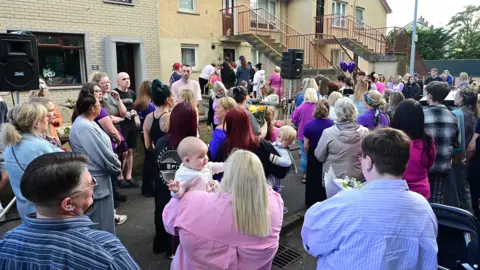 Pacemaker A large group of people standing around outside a residential property. 