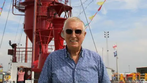 Johnnie Walker in a blue patterened shirt and dark sunglasses.