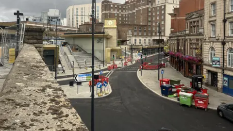 Eleanor Ingleby/BBC A view of Bishopgate Street from a nearby bridge. The road below has been recently resurfaced. To the left of the picture, the new steps leading up to Leeds railway station can be seen, with a new station clock behind. The Queen Hotel can be seen in the background.