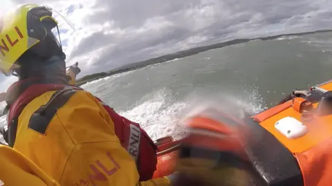 An RNLI rescue boat with a man in yellow waterproofs pointing at something
