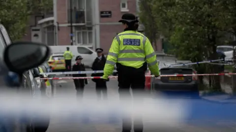PA Media Several police officers standing in Lord Warwick Street, a residential road, and several lines of police tape.
