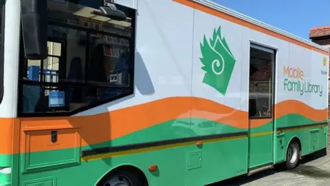 An orange, green and white bus with mobile family library written on the side.
