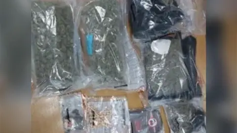 Plastic bags of what appears to be cannabis and other items are laid out on a wooden table.