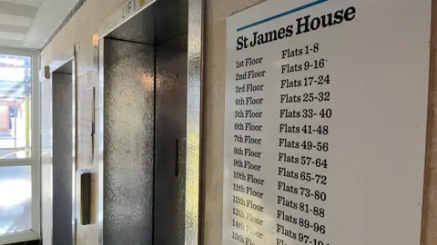 George Carden/BBC A sign that shows the flats from the first floor to 15th floor with two elevators behind them