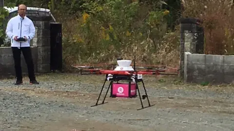 Lawson A man stands behind a drone sitting on the ground, which can deliver food to people in Japan