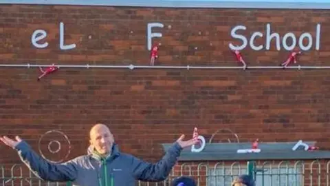 Amble Links Primary School Mr Heeley is throwing his arms up in mock-exasperation as the toy elves appear to have taken letters off the school sign, until they spelt: "eLF School".