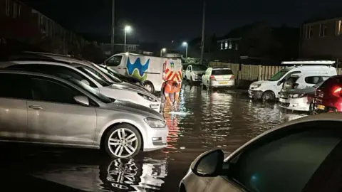 Jacob Cousins Picture shows flooding in a residential street. Welsh water engineer stands in front of a Welsh Water van working to sort the problem. 