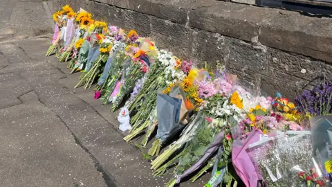Bunches of flowers in a long line on a pavement near the scene of the incident