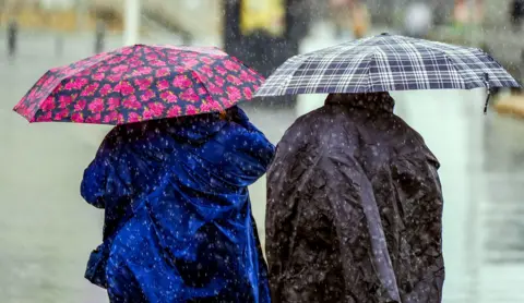 Two people hudlde underneath umbrellas