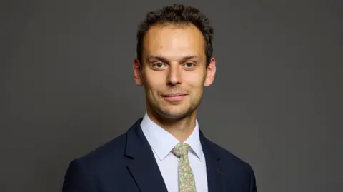 UK Parliament A headshot of Josh Simons who wears a dark suit and a colourful tie
