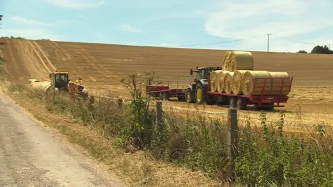 Two tractors moving hay bales in the bright sunshine.