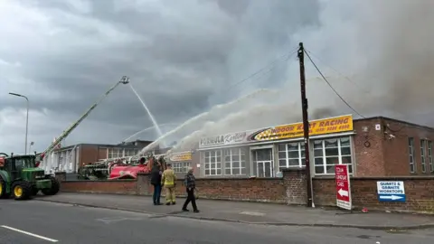 A tractor and fire engines blast water into the building