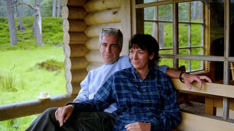 US Department of Justice An undated photo released by the US justice department shows Jeffrey Epstein and his co-conspirator Ghislaine Maxwell seated close together outside a wooden home, appearing to be a cabin of some kind in a wooded area. 