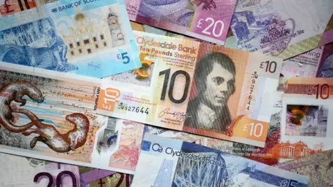 PA Media Scottish bank notes of various values and colours, laid out on a flat surface. 