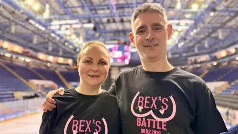 A man and a woman looking at the camera and smiling. They are wearing black, pink and white ice hockey jerseys.