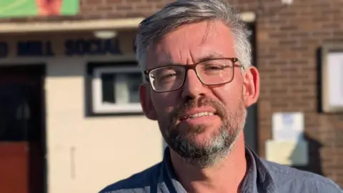 Councillor Barry Parsons, who has short grey hair, a beard and glasses, is outside a social club in Bristol.