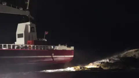 Kyle RNLI A red and white cargo vessel next to rocks on the Isle of Skye