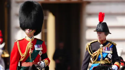 PA Media The Duke of Edinburgh, wearing a red military uniform, and the Princess Royal, in a black uniform, leave Buckingham Palace ahead of Trooping the Colour ceremony in central London