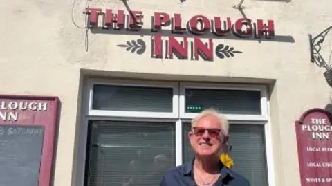 Chris Dean wears sunglasses as he stands in front of the Plough Inn in Guernsey 