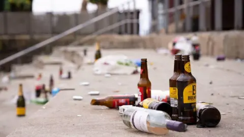 Getty Images A number of glass bottles can be seen scattered on a set of steps. There is wine bottle in the foreground alongside a few cider bottles. Just behind them, a smashed Budweiser beer bottle can be seen.