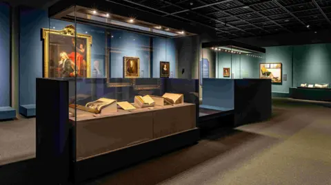 Wordsworth Grasmere A glass display case inside Busan Museum in South Korea containing books, one of which is the manuscript of a Wordsworth poem. Behind the glass case is a blue wall where paintings are hanging displayed in golden frames.