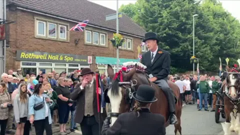 A man in a suit and top hat on a horse in a middle of parade