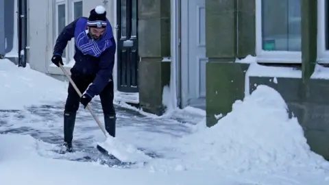 PA Media/Owen Humphreys A man shovels snow in Tow Law