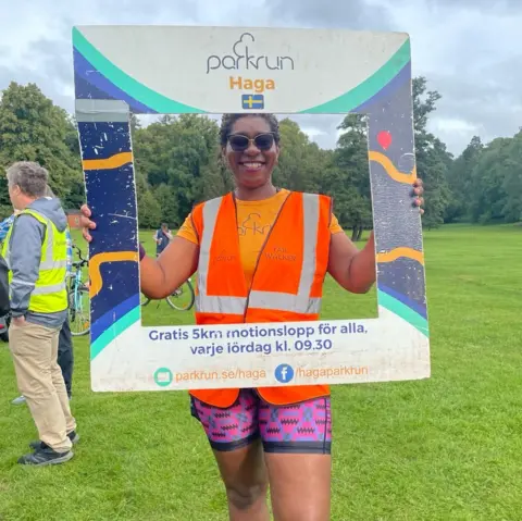 Parkrun Afe Komolafe holds a square Parkrun sign in Sweden