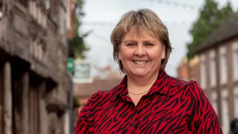 Woman wearing red and black zebra print blouse, smiling, with a blurred town centre behind her.