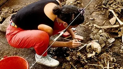 A woman examining bones in a mass grave