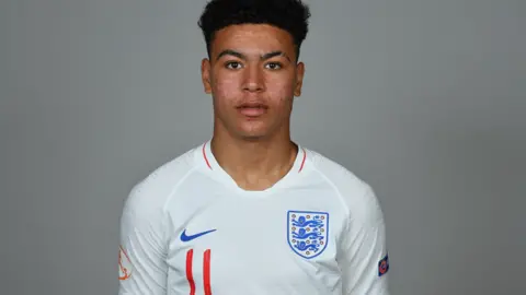 Getty Images Morgan Rogers is looking straight at the camera wearing a white England top. He is not smiling and the background is grey. 