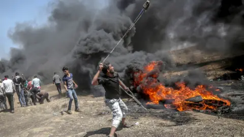EPA A Palestinian protester throws stones at Israeli troops during clashes after protests near the border with Israel in the east of Gaza Strip