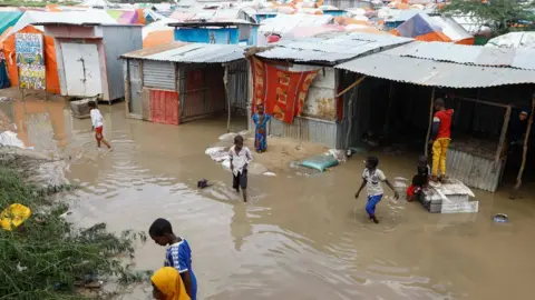 Reuters Children wading through flood water at a camp with makeshift huts for internally displaced people in Somalia