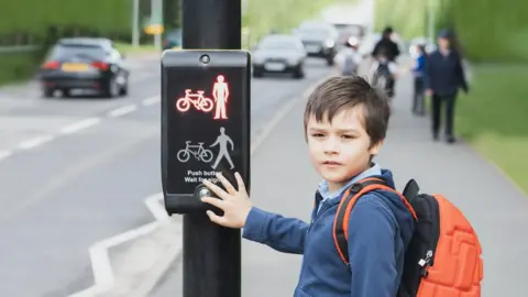 Getty Images Schoolboy pressing a button at traffic lights on pedestrian crossing on way to school (stock image)