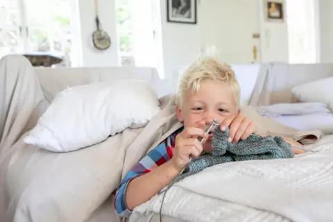 Karin Schermbrucker / Unicef A boy lies on a bed and does some knitting