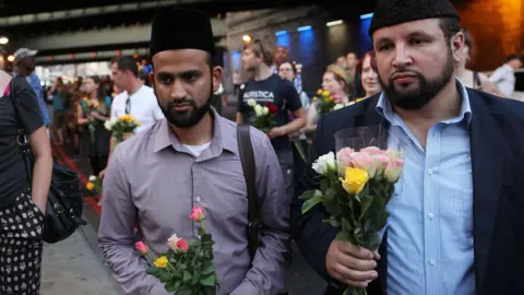 Getty Images Men bring flowers to the vigil in Finsbury Park