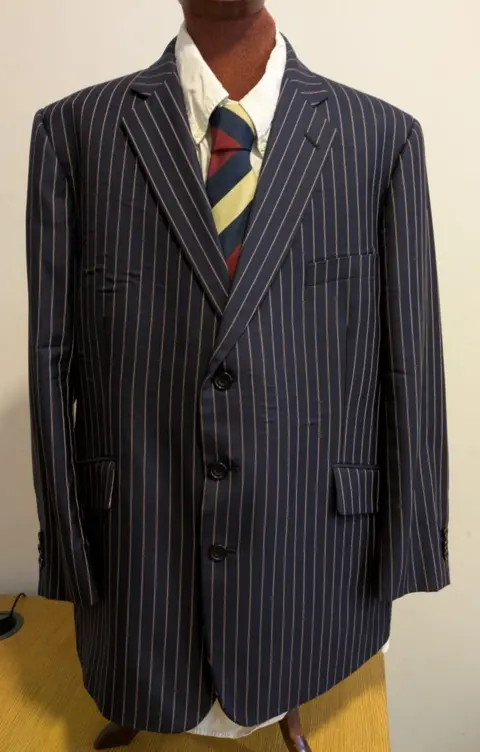 Boston Borough Council A black and white pinstripe suit jacket, white shirt, and blue, red and yellow tie on a mannequin. 