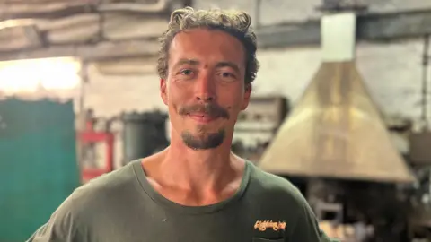Man stood in front of a furnace. 