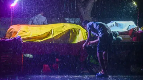Getty Images Street vendor trying to protect his shop with yellow covering during rain on May 21, 2025 in Noida, India.