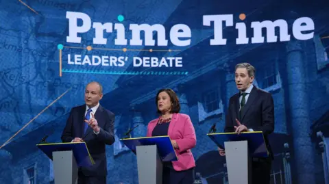 PA Media Michael Martin, Mary Lou McDonald and Simon Harris all stand at the podium during the debate