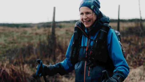 Clo Cam / Montane Winter Spine Race Runner Anna Troup on the Montane Winter Spine Race. She is wearing a blue waterproof jacket and a blue buff. She has a fell running backpack on and is holding blue running poles.
