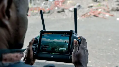 Getty Images The hand of a Congolese soldier holds the controls for a drone. It has two antennae and its screen shows a view of hills in eastern DR Congo