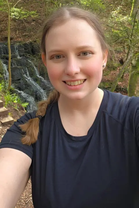 Hannah Long Hannah Long takes a selfie smiling at the camera. She has light brown hair which is plaited and sits on her left hand shoulder and smiles 