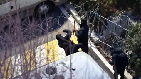 Police officers cut a wire fence set up at the entrance to the official residence of impeached South Korean President Yoon Suk Yeol, as authorities seek to execute an arrest warrant, in Seoul, South Korea, January 15, 2025.