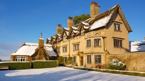The outside of How Hill House near Ludham. The building is set on acres of land and was built in the 1900s. The picture has been taken during the winter as snow dusts the tops of the house and the landscape.
