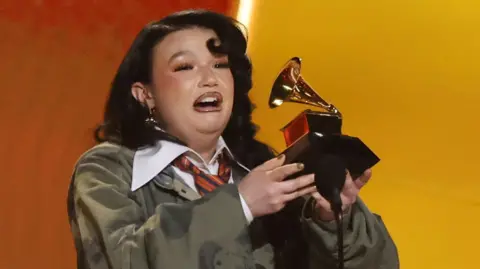 Reuters Lola Young on stage at the Grammys, holding up her trophy and giving her speech with an emotional expression