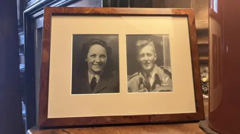 Kit Taylor/BBC via Beningbrough Hall A photo frame with black and white headshots of a woman on the left hand side and a man on the right, in a dark oak frame. 