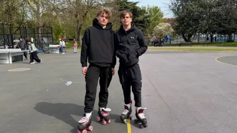 BBC Leo and Noah in black tracksuits and roller-skates. 