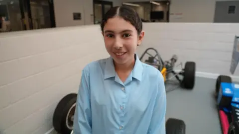 Student Karma smiling for the camera. There are racing cars behind her.